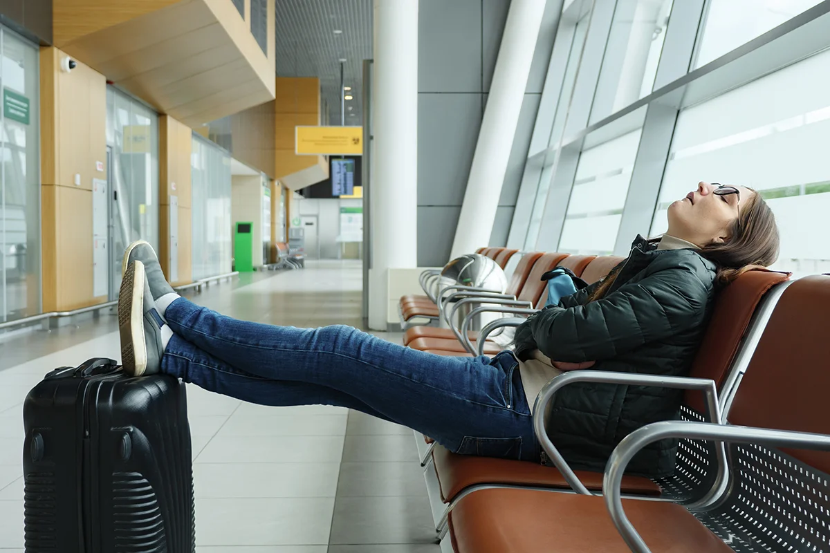 Bored and tired young woman is waiting her flight in airport sitting in hall.